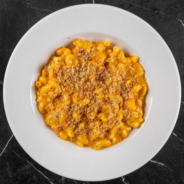 Macaroni and cheese in a white bowl, topped with breadcrumbs, on a dark marble table.