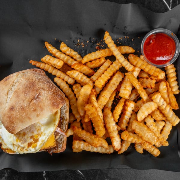 Sandwich with fried egg and cheese, crinkle-cut seasoned fries, and ketchup on a black tray.