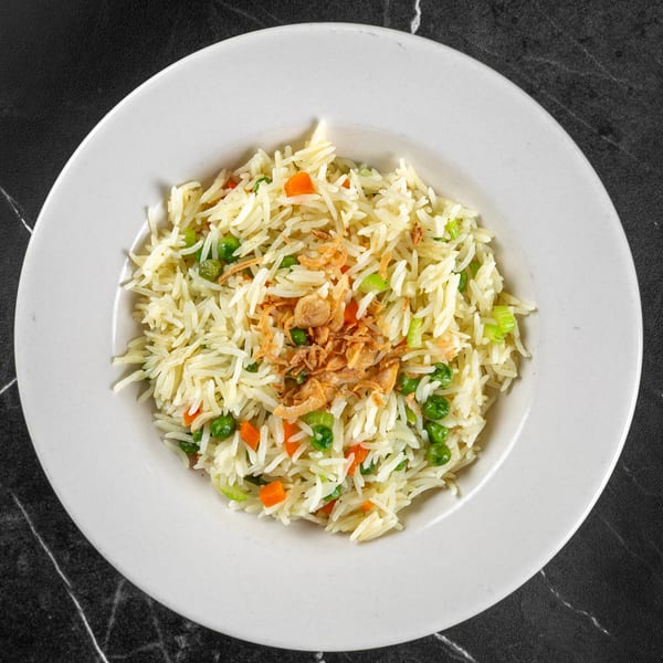 Overhead view of vegetable fried rice topped with crispy onions on a white plate.