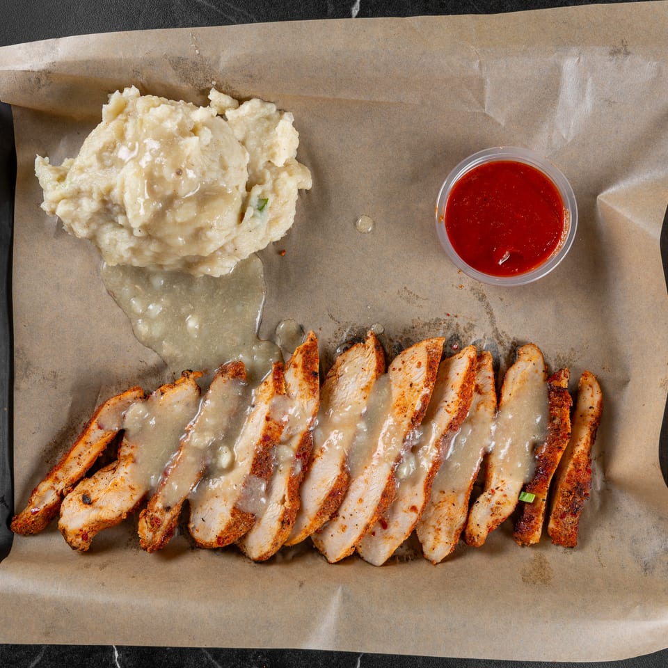 Seasoned chicken slices with gravy, mashed potatoes, and a side of red sauce.