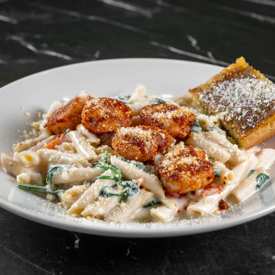 Creamy penne pasta with breaded shrimp, spinach, and a side of garlic bread on a white plate.