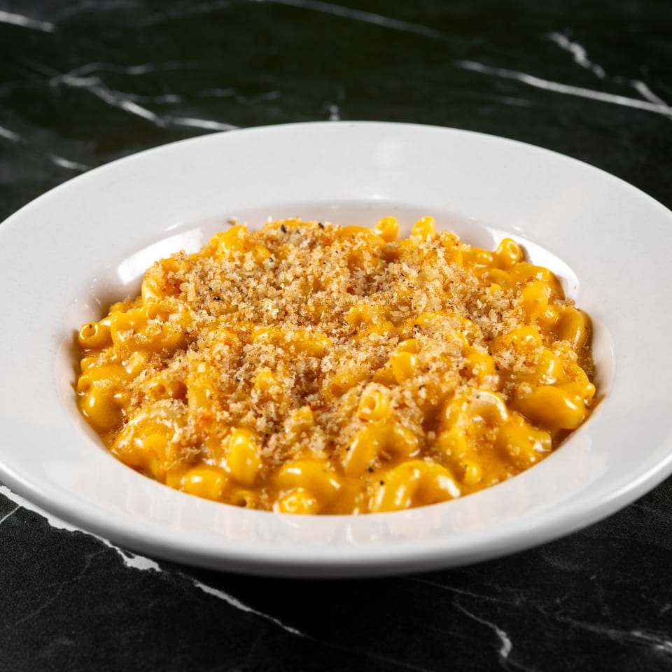 A white bowl of creamy mac and cheese with a golden-brown breadcrumb topping on a dark marble surface.